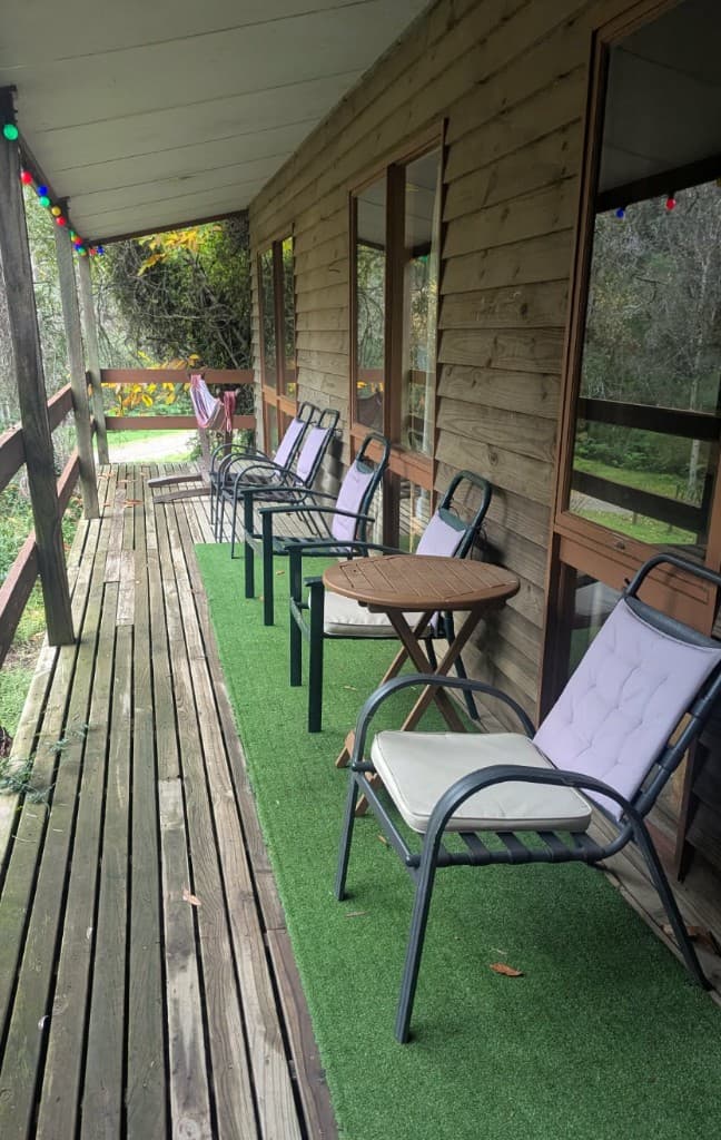 A covered wooden porch with cushioned chairs and festoon lights at Charnwood Campground