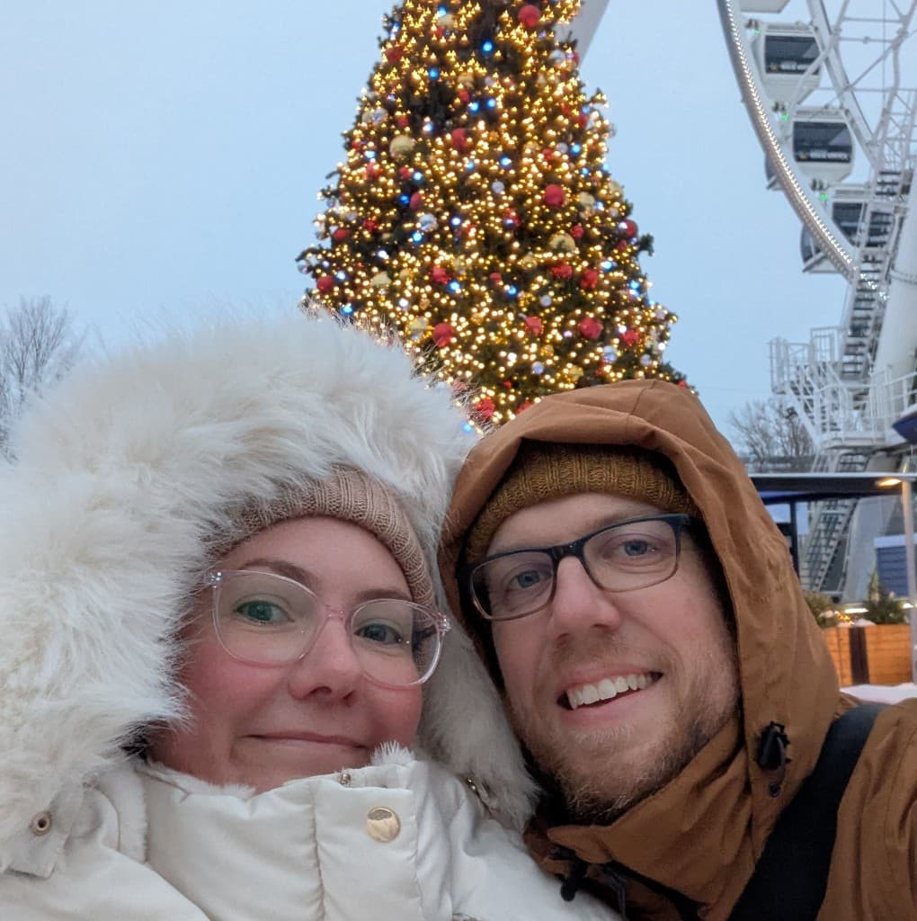 Leigh and Tom rugged up in front of Christmas lights and a ferris wheel